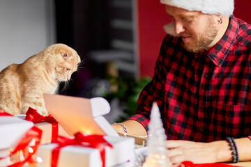 Vet Man in Santa hat and cat in hand making greeting card for New Year and Christmas