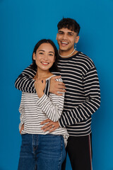 Wall Mural - Young smiling stylish guy hugging his happy beautiful asian girlfriend