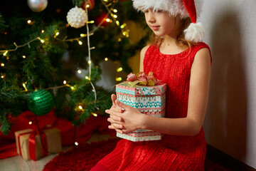 Wall Mural - Cute girl hold gifts, present box near christmas tree in the morning at home