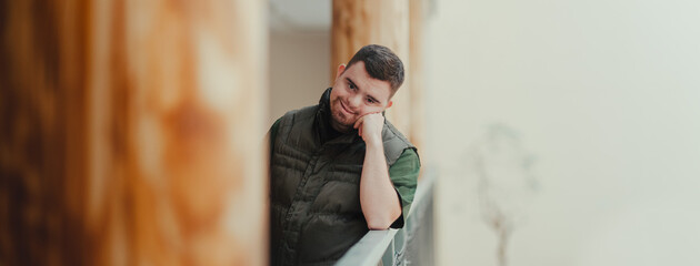 Portrait of young pensive man with down syndrome, resting after cleaning animal enclosure in zoo. Concept of integration people with disabilities into society.