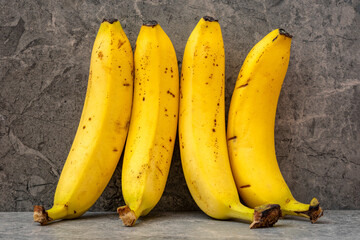 Wall Mural - Four yellow bananas leaning on a grey stone background