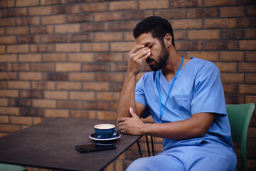 Tired caregiver man resting outdoor, in front of nurishing home.