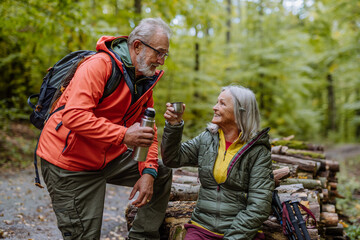 Wall Mural - Senior couple having break during hiking in autumn forest.