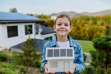 Wall Mural - Close up of happy little girl holding paper model of house with solar panels.Alternative energy, saving resources and sustainable lifestyle concept.