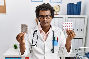 Poster - African man wearing doctor uniform holding prescription pills relaxed with serious expression on face. simple and natural looking at the camera.