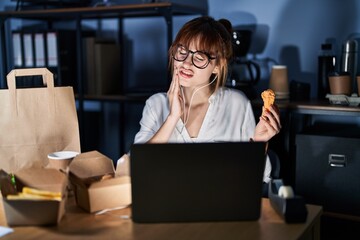 Poster - Young beautiful woman working using computer laptop and eating delivery food touching mouth with hand with painful expression because of toothache or dental illness on teeth. dentist concept.