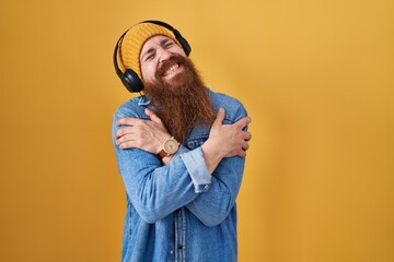 Poster - Caucasian man with long beard listening to music using headphones hugging oneself happy and positive, smiling confident. self love and self care