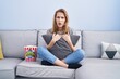 © Krakenimages.com - Beautiful blonde woman watching tv sitting on the sofa in shock face, looking skeptical and sarcastic, surprised with open mouth