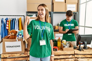 Canvas Print - Young blonde girl wearing volunteer t shirt at donation stand smiling with happy face looking and pointing to the side with thumb up.