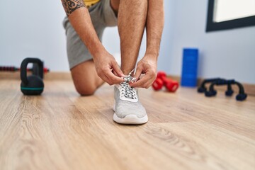 Poster - Young hispanic man tying shoe at sport center