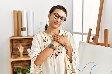 Poster - Young hispanic woman with short hair at art studio smiling with hands on chest with closed eyes and grateful gesture on face. health concept.