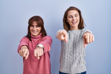 Sticker - Mother and daughter standing over blue background pointing to you and the camera with fingers, smiling positive and cheerful