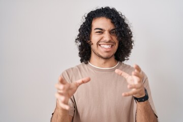 Wall Mural - Hispanic man with curly hair standing over white background shouting frustrated with rage, hands trying to strangle, yelling mad