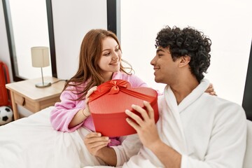 Wall Mural - Young couple smiling happy holding valentine heart box gift at bedroom.