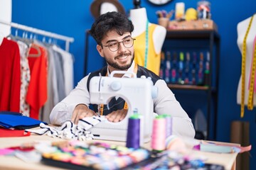 Wall Mural - Young hispanic man tailor smiling confident using sewing machine at sewing studio