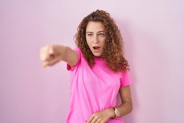 Sticker - Young caucasian woman standing over pink background pointing with finger surprised ahead, open mouth amazed expression, something on the front