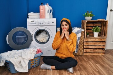 Poster - Young hispanic woman doing laundry laughing and embarrassed giggle covering mouth with hands, gossip and scandal concept