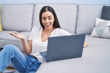 Canvas Print - Young brunette woman using laptop at home celebrating achievement with happy smile and winner expression with raised hand