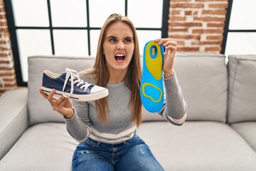 Wall Mural - Young woman holding shoe insole angry and mad screaming frustrated and furious, shouting with anger. rage and aggressive concept.