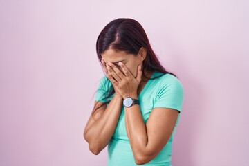 Poster - Young hispanic woman standing over pink background with sad expression covering face with hands while crying. depression concept.