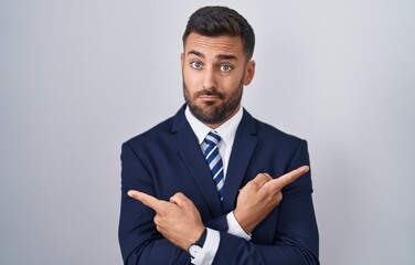 Handsome hispanic man wearing suit and tie pointing to both sides with fingers, different direction disagree