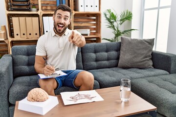 Wall Mural - Handsome hispanic man working with rorschach test at psychology clinic pointing to you and the camera with fingers, smiling positive and cheerful