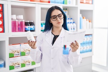 Wall Mural - Young caucasian woman pharmacist holding pills bottle reading prescription at pharmacy