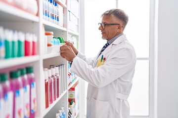 Poster - Middle age grey-haired man pharmacist holding deodorant bottle at laboratory