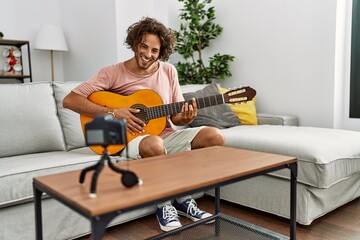 Canvas Print - Young hispanic man recording with camera playing classical guitar at home.