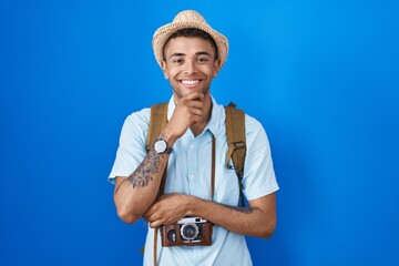 Canvas Print - Brazilian young man holding vintage camera looking confident at the camera smiling with crossed arms and hand raised on chin. thinking positive.