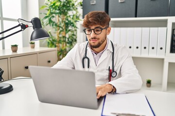 Wall Mural - Young arab man wearing doctor uniform using laptop working at clinic