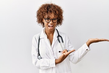 Wall Mural - Young african american woman wearing doctor uniform and stethoscope amazed and smiling to the camera while presenting with hand and pointing with finger.