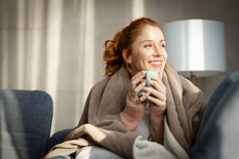 Woman With Blanket Over Shoulders, Siting On Bed By The Window In Casual Clothes Enjoying Her Morning Coffee