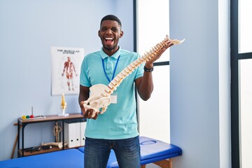 Wall Mural - African american man holding anatomical model of spinal column celebrating crazy and amazed for success with open eyes screaming excited.