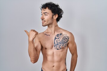 Poster - Hispanic man standing shirtless smiling with happy face looking and pointing to the side with thumb up.