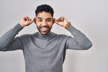 Canvas Print - Hispanic man with beard standing over white background smiling pulling ears with fingers, funny gesture. audition problem