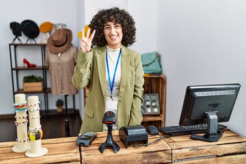 Poster - Young middle eastern woman working as manager at retail boutique showing and pointing up with fingers number three while smiling confident and happy.