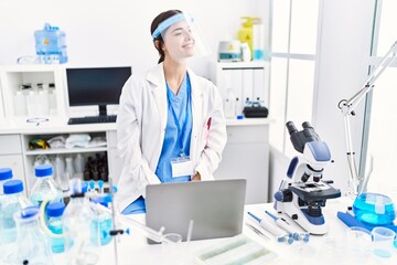 Poster - Young hispanic woman wearing scientist uniform looking away to side with smile on face, natural expression. laughing confident.