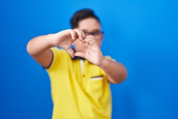 Sticker - Young hispanic kid standing over blue background smiling in love showing heart symbol and shape with hands. romantic concept.