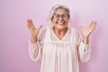 Poster - Middle age woman with grey hair standing over pink background celebrating mad and crazy for success with arms raised and closed eyes screaming excited. winner concept