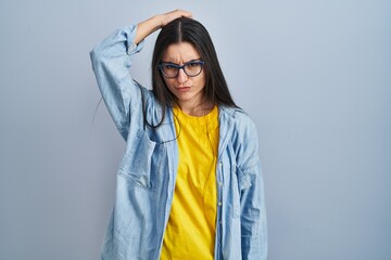 Poster - Young hispanic woman standing over blue background confuse and wondering about question. uncertain with doubt, thinking with hand on head. pensive concept.