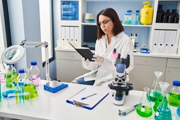 Wall Mural - Young beautiful hispanic woman scientist reading book at laboratory