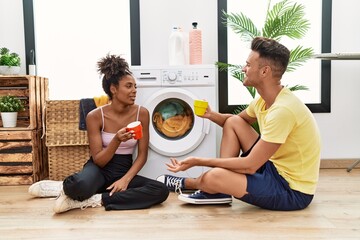 Canvas Print - Man and woman couple drinking coffee waiting for washing machine at laundry room