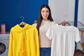 Poster - Young woman hanging clothes on racks sticking tongue out happy with funny expression.