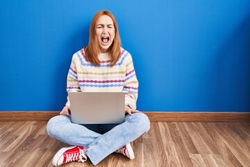 Sticker - Young woman using laptop at home sitting on the floor angry and mad screaming frustrated and furious, shouting with anger. rage and aggressive concept.