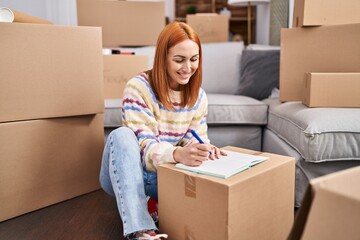 Wall Mural - Young caucasian woman smiling confident writing on notebook at new home