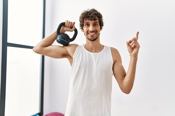 Canvas Print - Young hispanic man wearing sportswear using dumbbells smiling happy pointing with hand and finger to the side