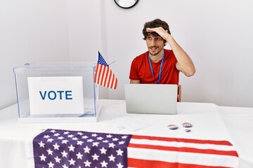 Sticker - Young hispanic man at political election sitting by ballot very happy and smiling looking far away with hand over head. searching concept.