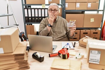 Wall Mural - Senior caucasian man working at small business ecommerce holding shopping cart covering mouth with hand, shocked and afraid for mistake. surprised expression