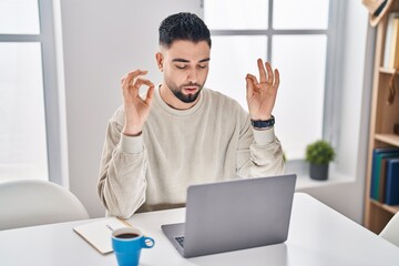 Sticker - Young arab man doing yoga exercise sitting on table working at home